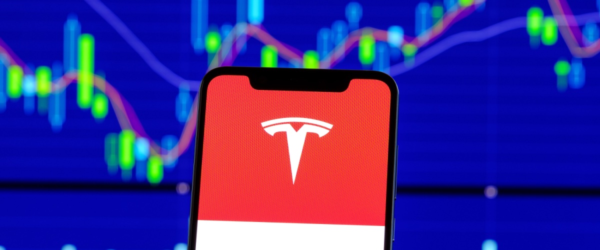 A mobile phone displaying the Tesla logo, with a stock chart in the background