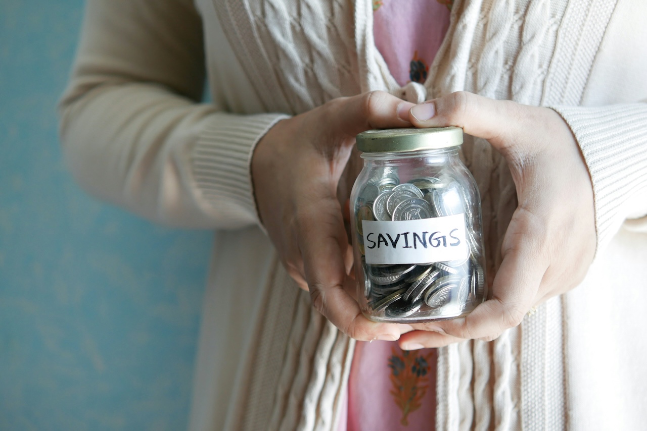 A photo of someone holding a jar of coins marked savings.